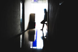 photo - Woman Standing at the End of a Dark Corridor